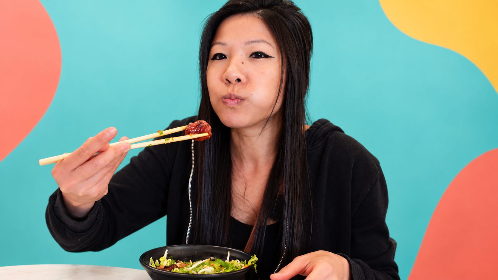Hong holding a bite of pork sausage with chopsticks